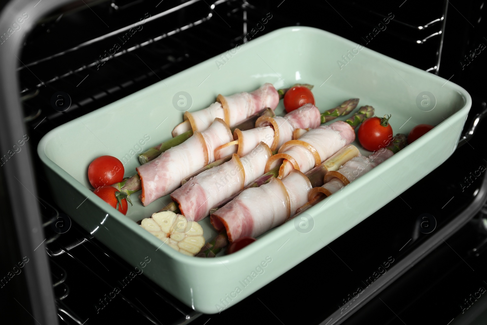 Photo of Uncooked bacon wrapped asparagus in baking dish on oven rack, closeup