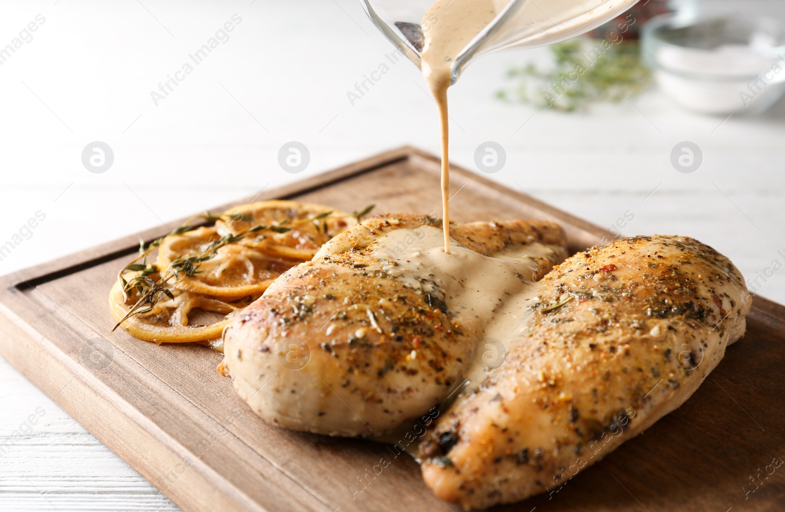 Photo of Pouring sauce onto baked lemon chicken on white wooden table