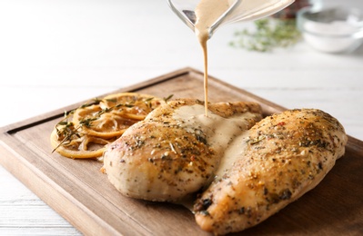 Photo of Pouring sauce onto baked lemon chicken on white wooden table