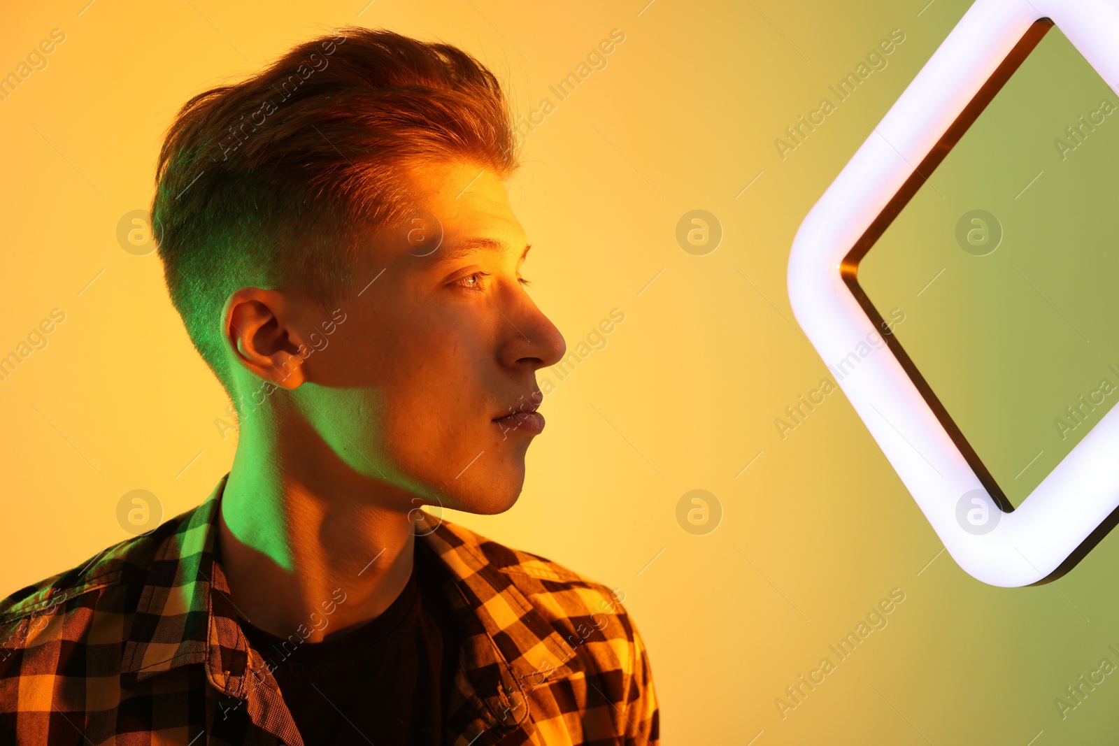 Photo of Young man with square lamp on color background in neon lights