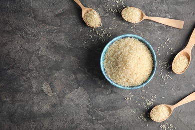 Photo of Bowl and spoons with uncooked rice on grey background, flat lay. Space for text