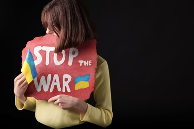 Photo of Woman holding poster with words Stop the War and Ukrainian flag on black background. Space for text