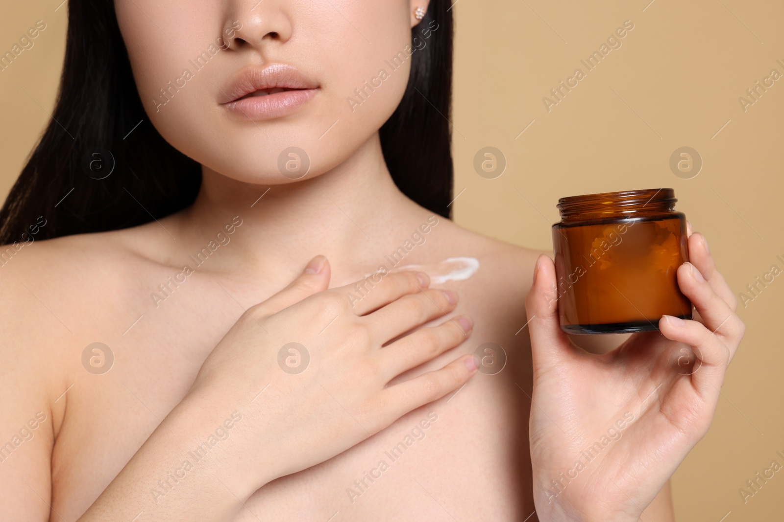 Photo of Beautiful young Asian woman with jar of body cream on beige background, closeup