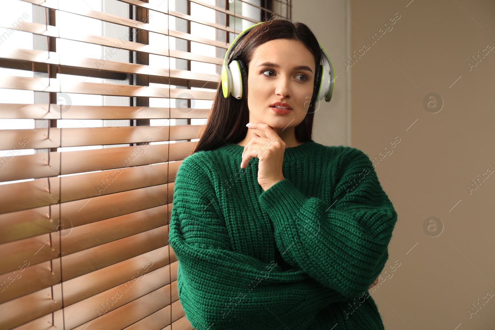 Photo of Young woman listening to audiobook near window indoors