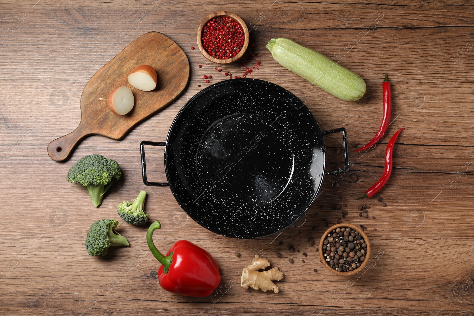 Photo of Empty iron wok surrounded by raw ingredients on wooden table, flat lay