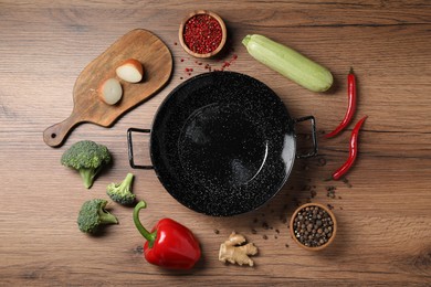 Photo of Empty iron wok surrounded by raw ingredients on wooden table, flat lay