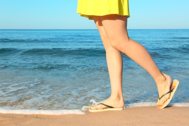 Photo of Closeup of woman with flip flops on sand near sea, space for text. Beach accessories