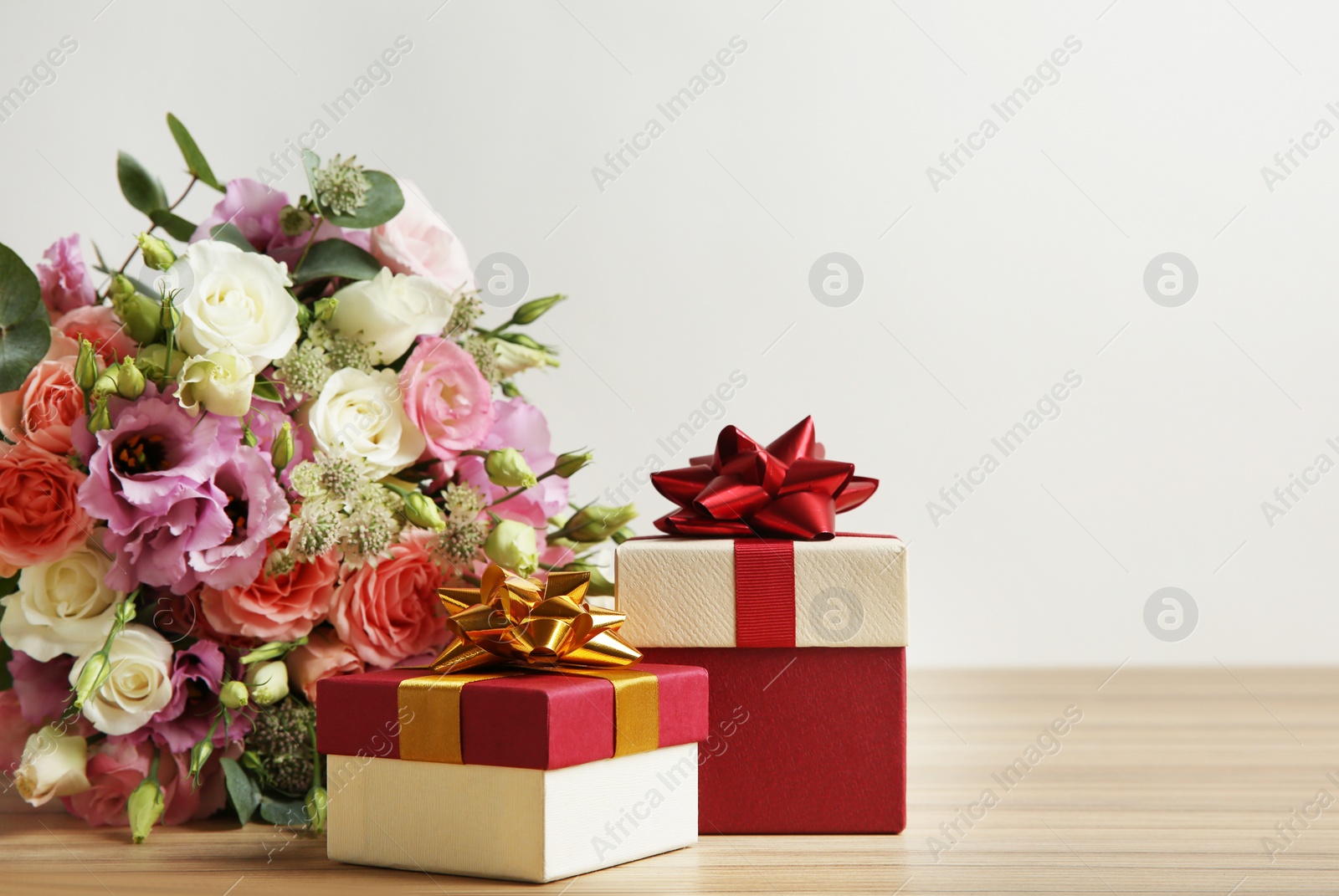 Photo of Beautiful bouquet of flowers and gift boxes on wooden table against light background. Space for text