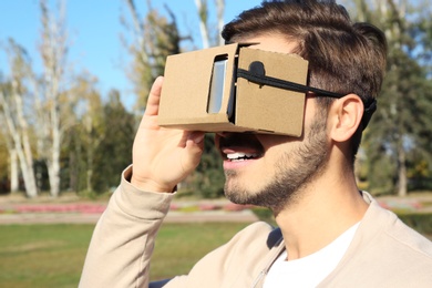 Photo of Young man using cardboard virtual reality headset outdoors