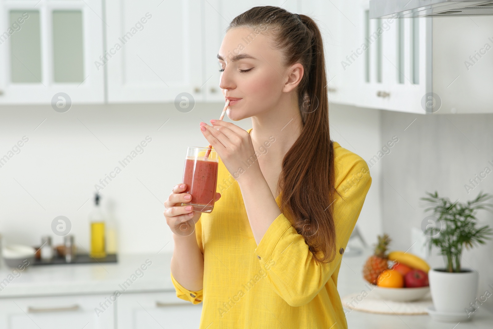 Photo of Beautiful young woman drinking delicious smoothie in kitchen