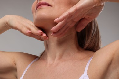 Woman touching her neck on grey background, closeup