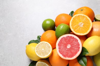 Photo of Pile of different fresh citrus fruits and leaves on grey textured table, flat lay. Space for text