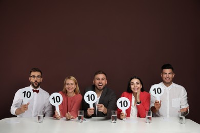 Photo of Panel of judges holding signs with highest score at table on brown background