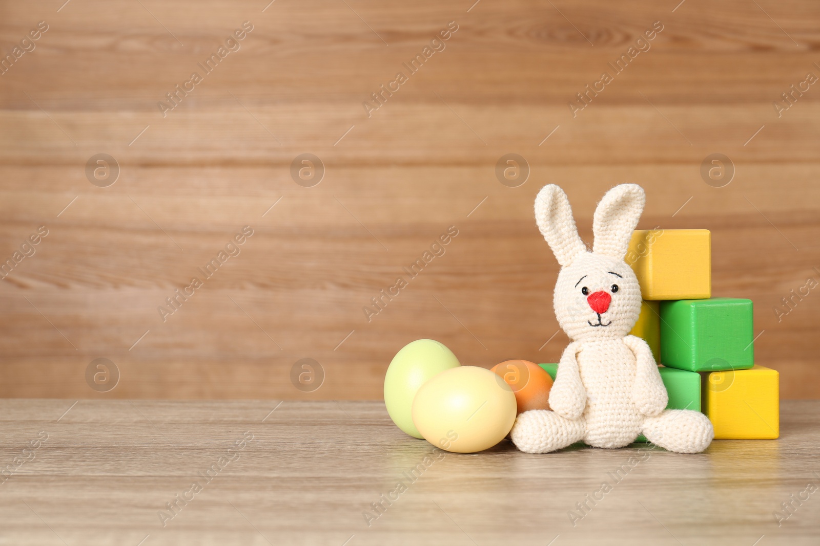 Photo of Cute Easter bunny toy near colorful cubes and dyed eggs on table, space for text