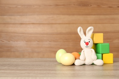 Cute Easter bunny toy near colorful cubes and dyed eggs on table, space for text