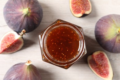 Photo of Jar of tasty sweet jam and fresh figs on white wooden table, flat lay