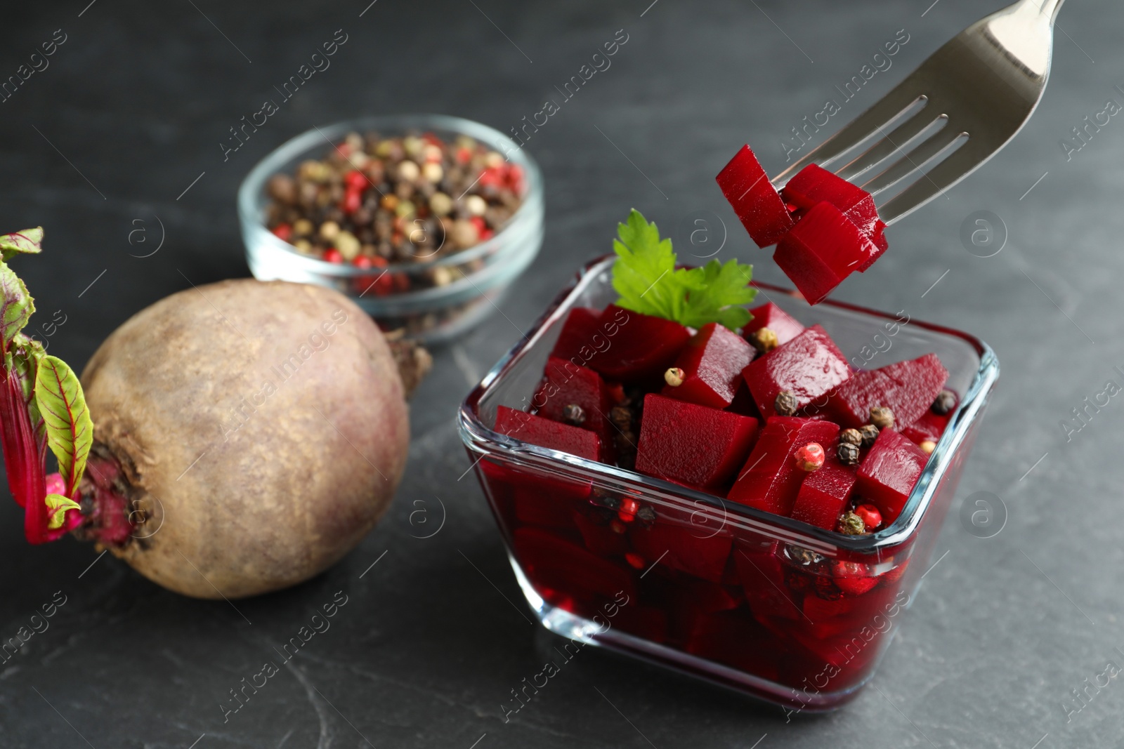 Photo of Pickled beets and fork over glass bowl on dark marble table