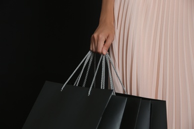 Photo of Young woman with shopping bags on dark background, closeup. Black Friday Sale