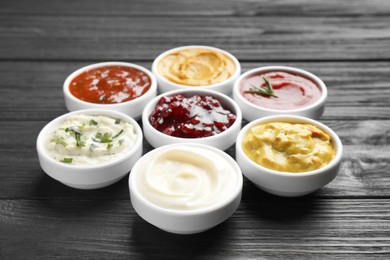 Photo of Different tasty sauces in bowls on black wooden table, closeup