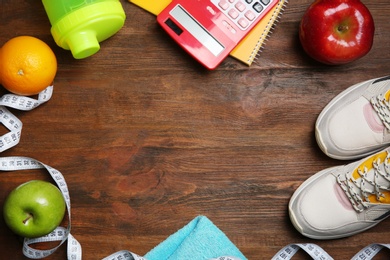 Photo of Flat lay composition with sneakers, healthy food, calculator and space for text on wooden background. Weight loss concept