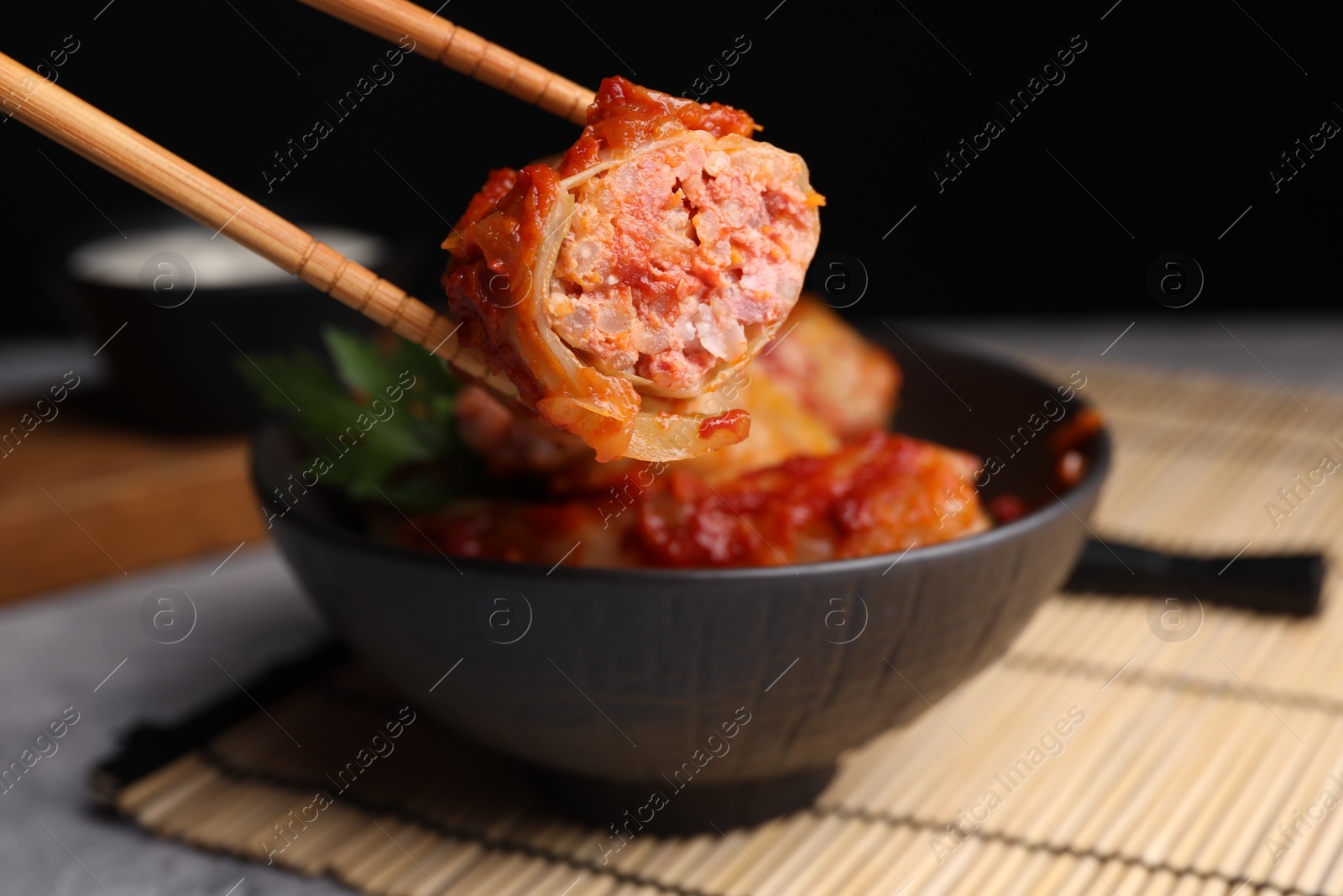 Photo of Taking delicious stuffed cabbage roll from bowl at table, closeup