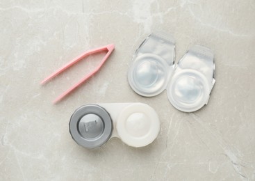 Packages with contact lenses, case and tweezers on light grey table, flat lay