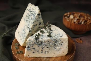 Photo of Tasty blue cheese with thyme on brown table, closeup
