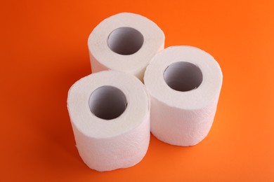 Photo of Soft toilet paper rolls on orange background, closeup