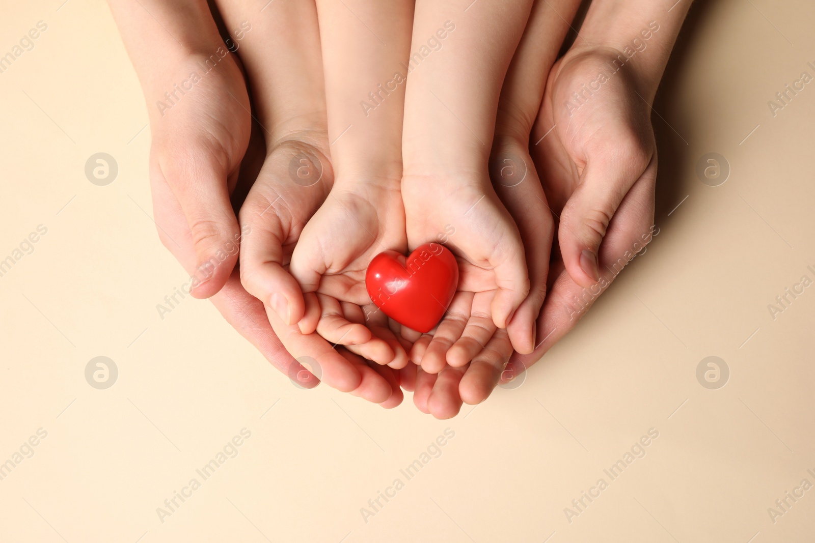 Photo of Parents and kid holding red heart in hands on beige background, top view