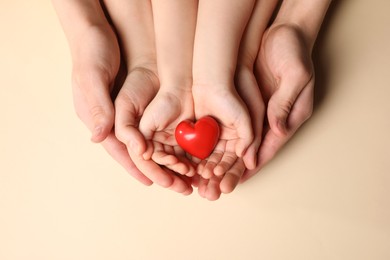 Photo of Parents and kid holding red heart in hands on beige background, top view