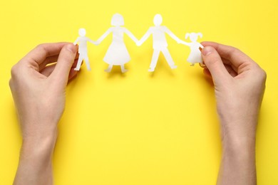 Woman holding paper cutout of family on yellow background, top view