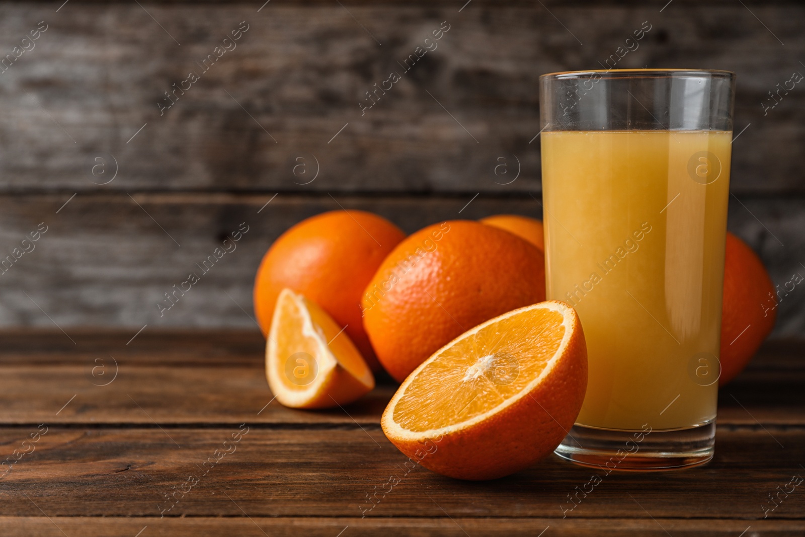 Photo of Glass of fresh juice and oranges on wooden table. Space for text