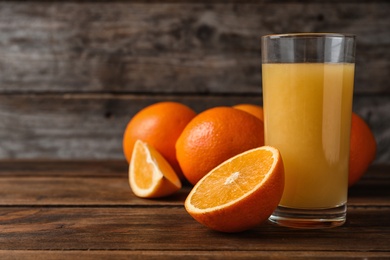 Photo of Glass of fresh juice and oranges on wooden table. Space for text