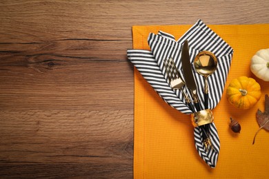 Photo of Cutlery, napkin and pumpkins on wooden background, flat lay with space for text. Table setting