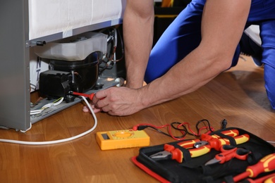 Photo of Male technician repairing broken refrigerator indoors, closeup