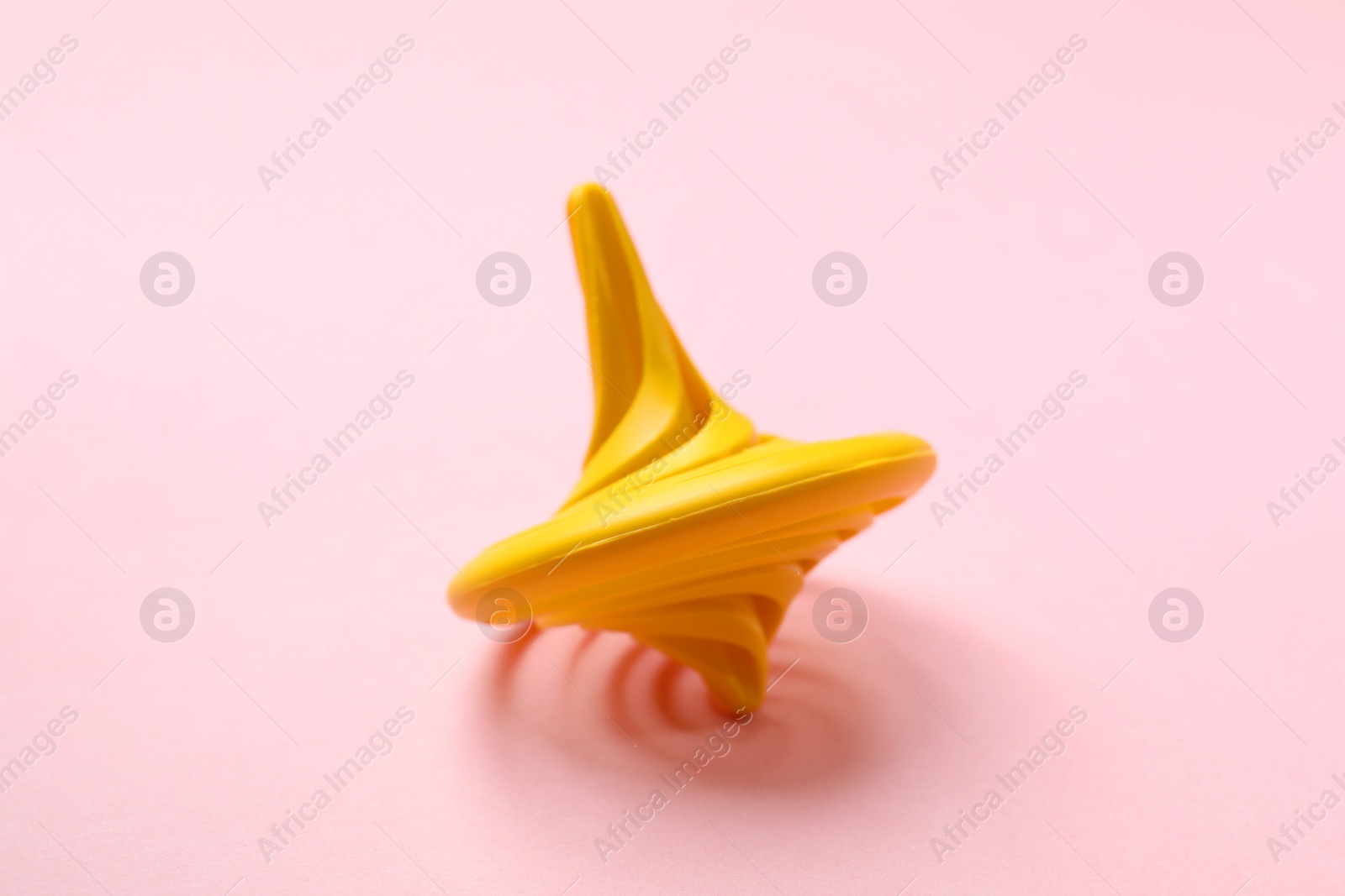 Photo of Yellow spinning top on pink background, closeup