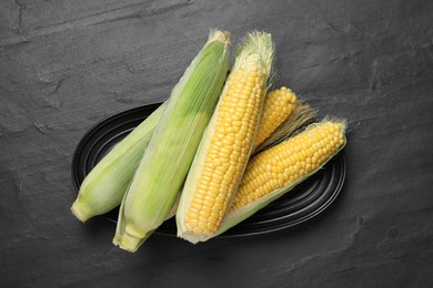 Photo of Fresh raw corn cobs on black table, top view