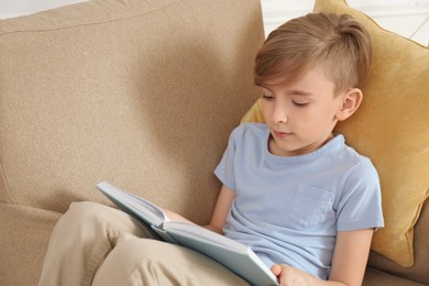 Photo of Little boy reading book in armchair at home