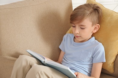 Little boy reading book in armchair at home