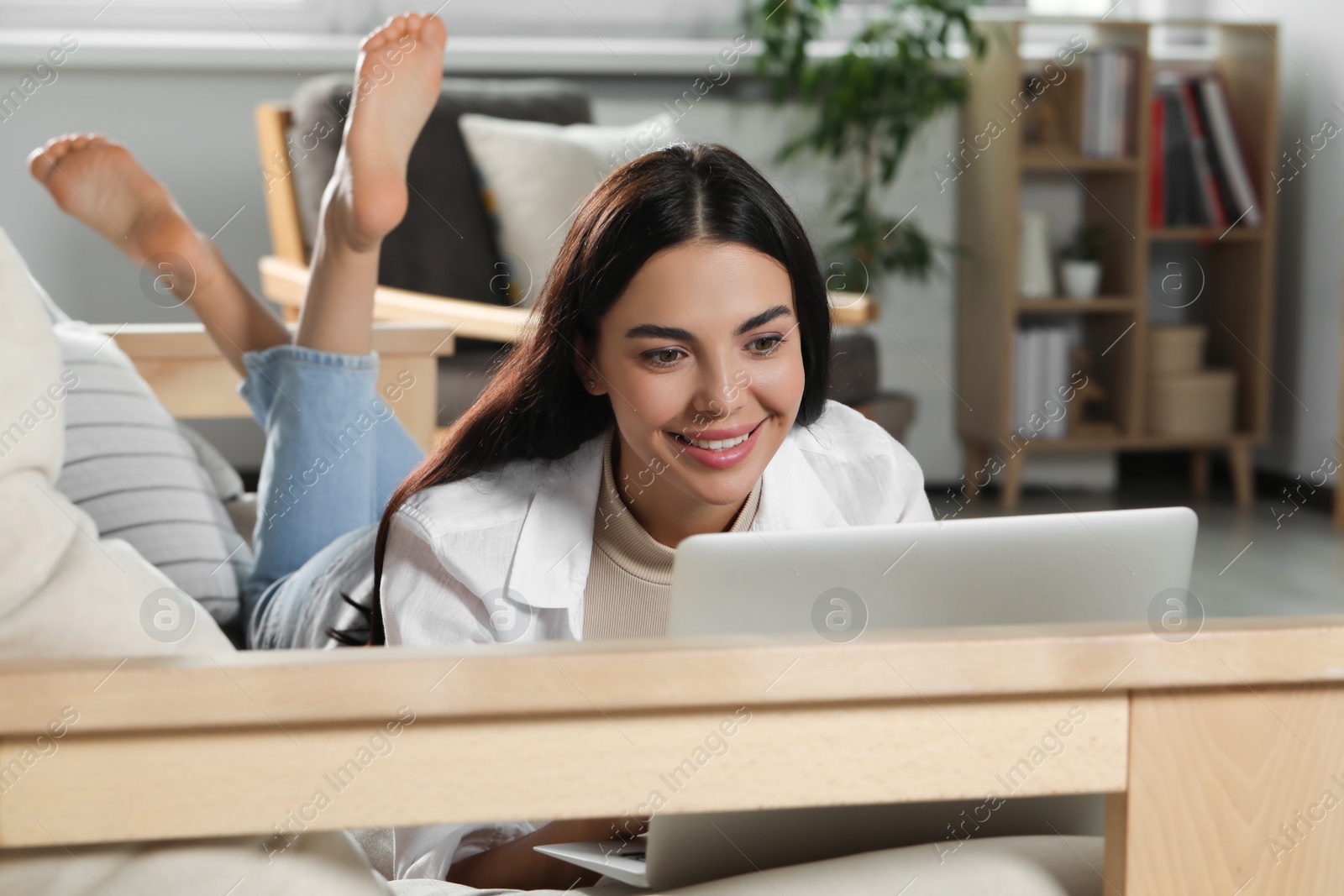 Photo of Young woman working with laptop on sofa at home