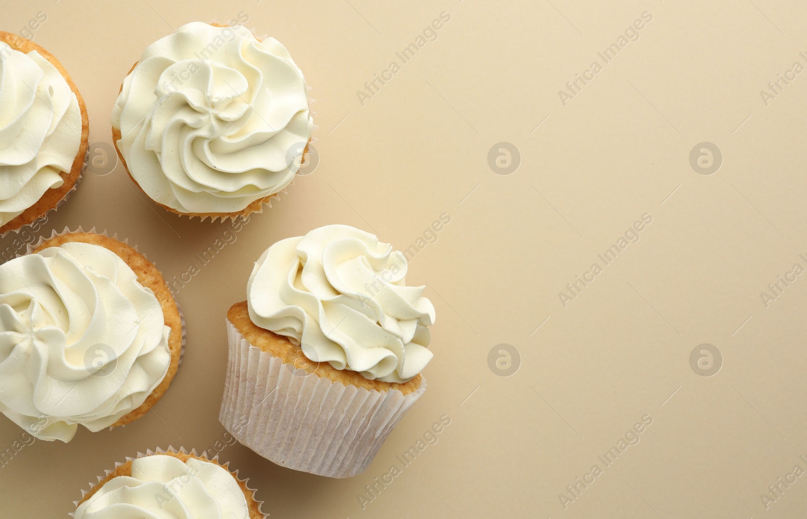 Photo of Tasty vanilla cupcakes with cream on beige background, top view. Space for text