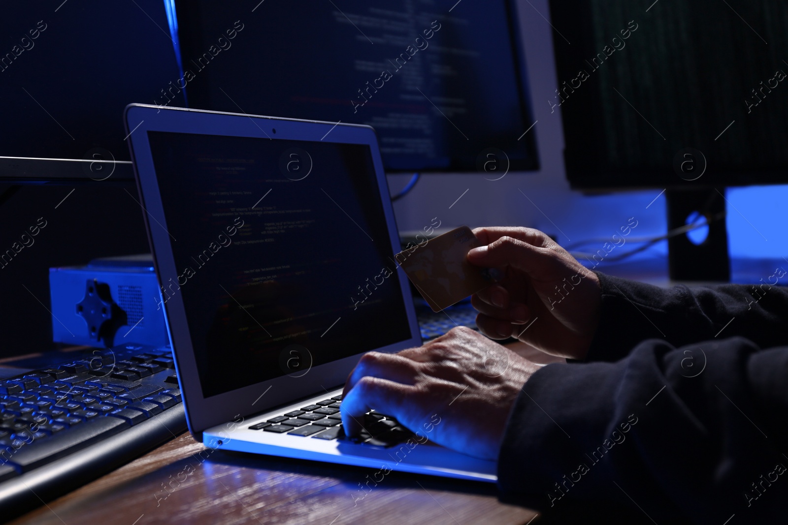 Photo of Hacker with computers and credit card in dark room, closeup. Cyber crime