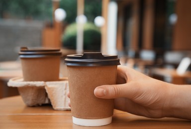 Woman with paper coffee cup at wooden table outdoors, closeup