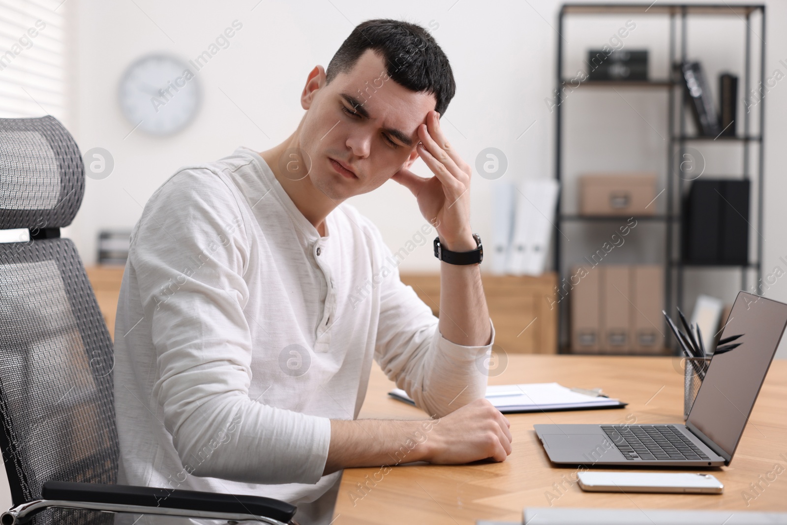 Photo of Young man suffering from headache at workplace in office