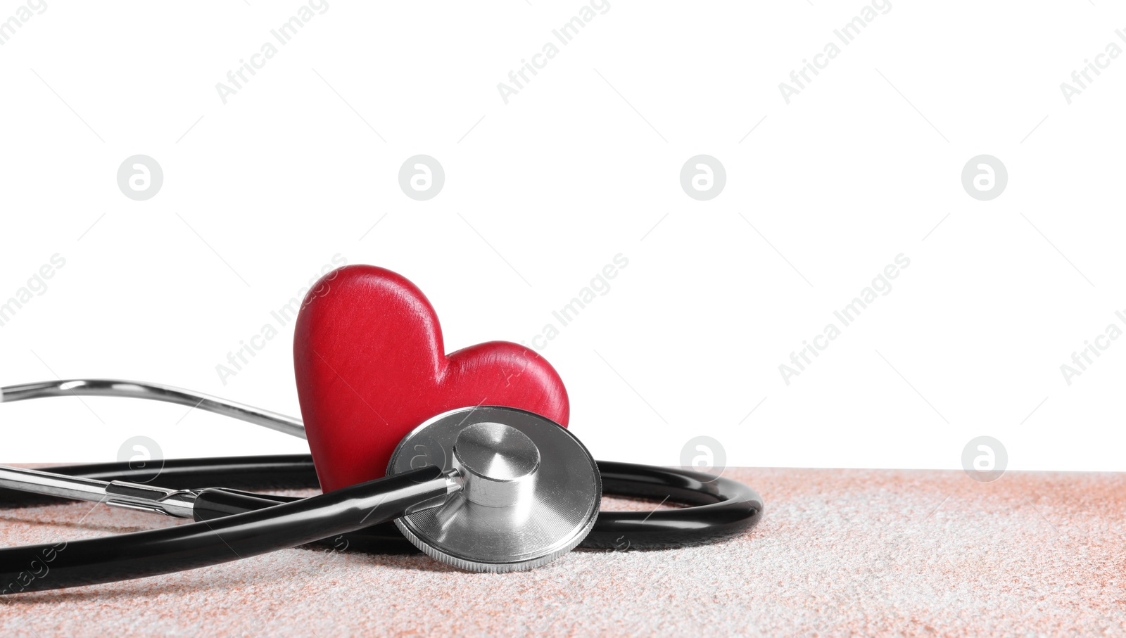 Photo of Stethoscope and red heart on color textured table against white background, space for text