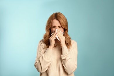 Photo of Woman with tissue suffering from runny nose on light blue background