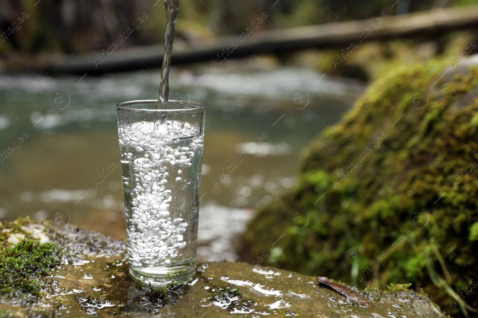 Photo of Fresh water pouring into glass on stone near river. Space for text