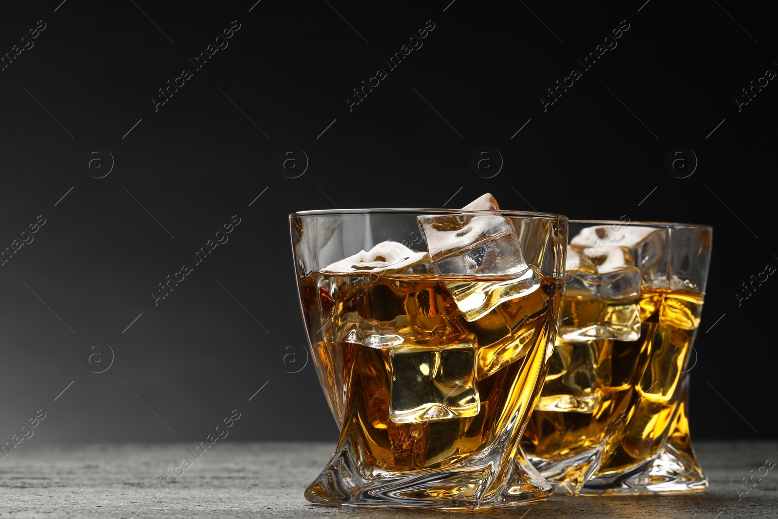 Photo of Whiskey and ice cubes in glasses on grey textured table, closeup. Space for text