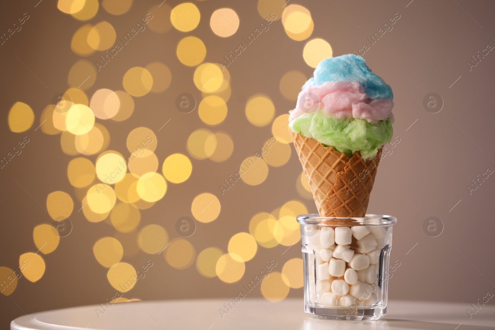 Photo of Sweet cotton candy in waffle cone on table against blurred lights, closeup. Space for text