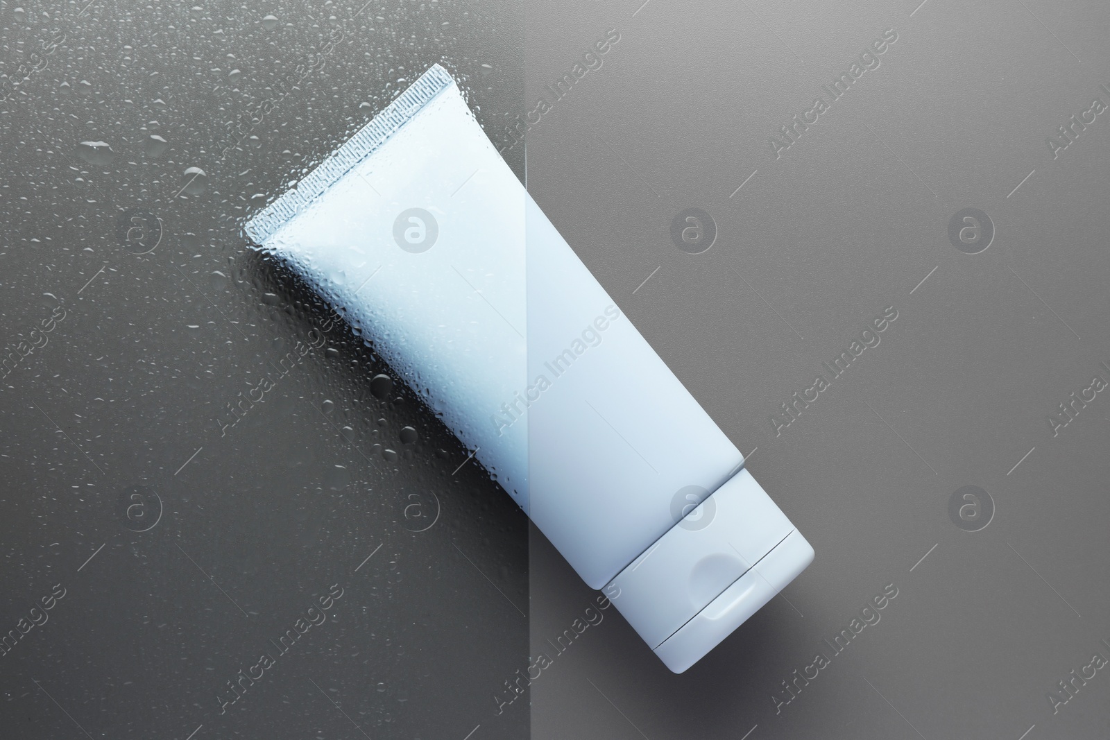 Photo of Tube with moisturizing cream on wet grey surface, top view